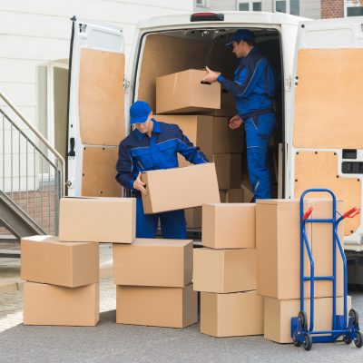 Young delivery men unloading cardboard boxes from truck on street